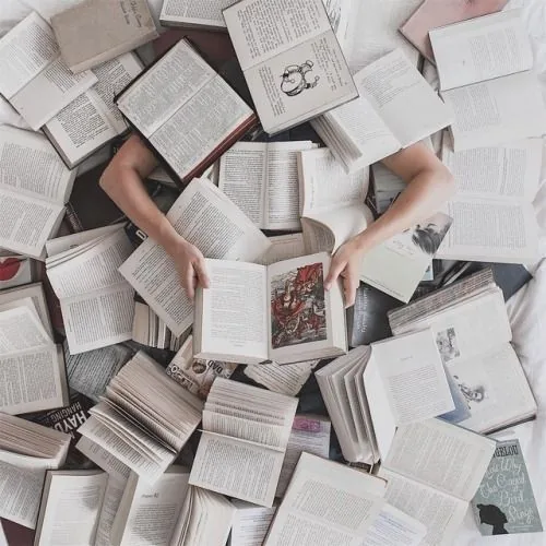 A reader lying among dozens of open books