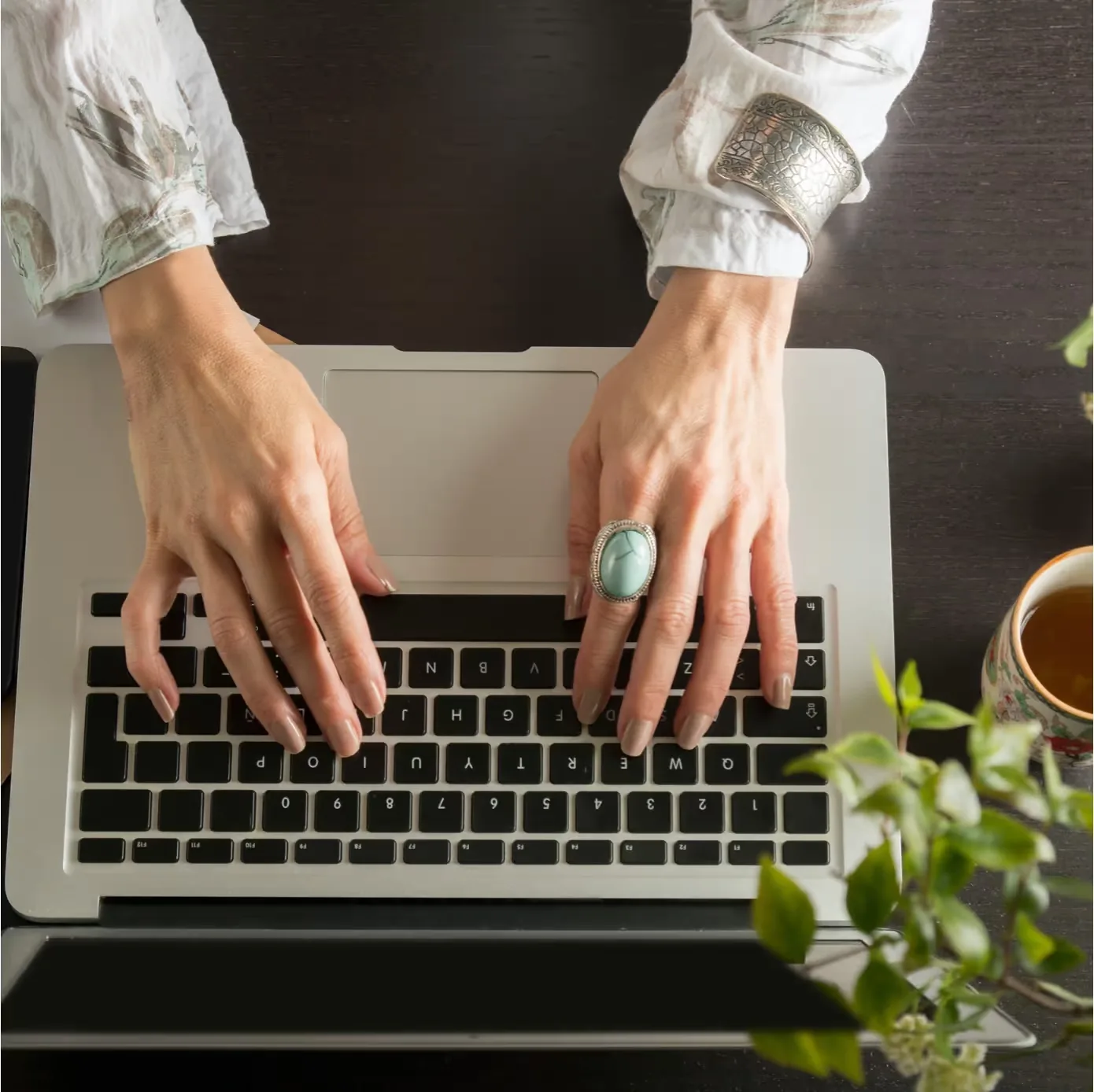 A writer typing on a laptop beside a cup of tea